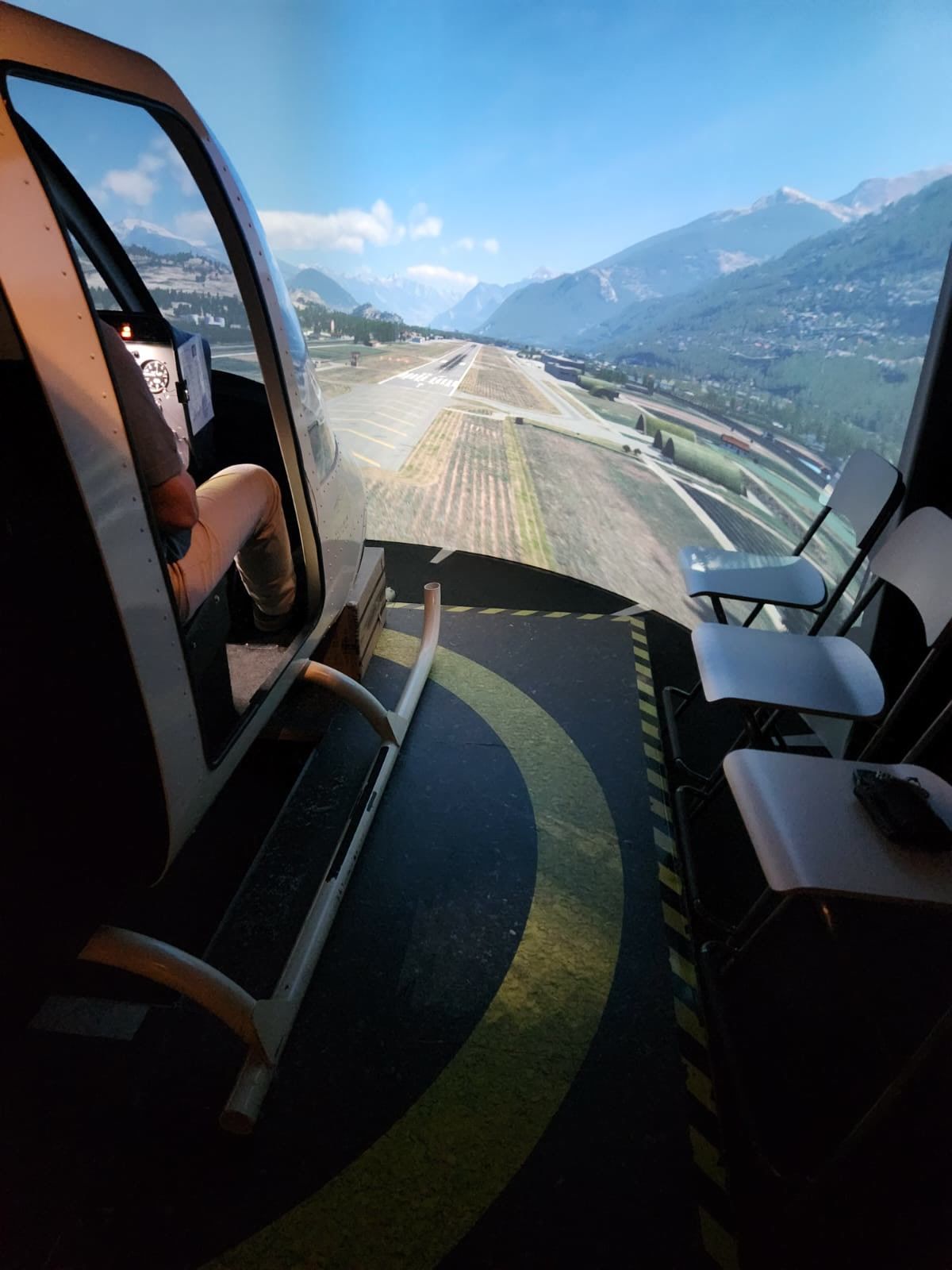 Seitlicher Blick in den Simulatorraum mit Cockpit, Projektionswand und Zuschauerplätzen.